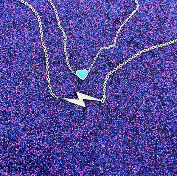 This is a photo of a blue heart necklace with a silver lightning bolt necklace on purple glitter