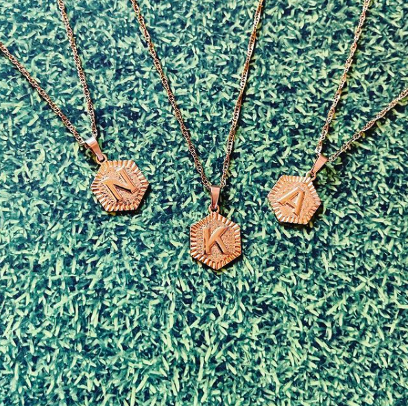 This is an image of our hexagon initial necklace in N K and A on a grass background