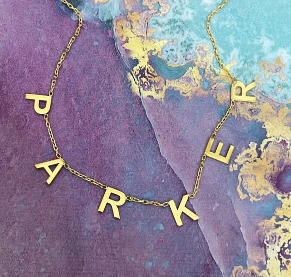 This is an image of our hanging name necklace PARKER on  a purple and blue marble background