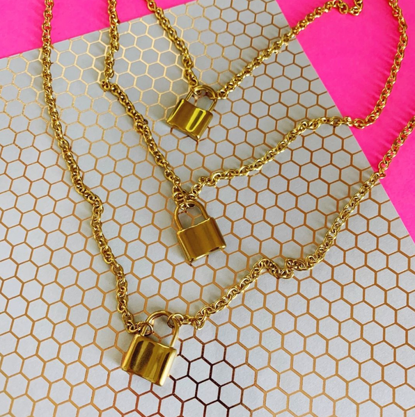This is an image of three gold chain lock necklaces on a pink and honeycomb background