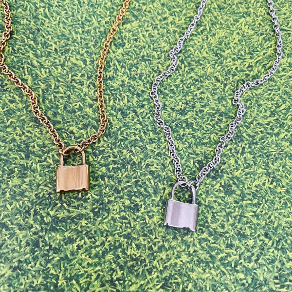 gold and silver lock pendant necklaces on grass background