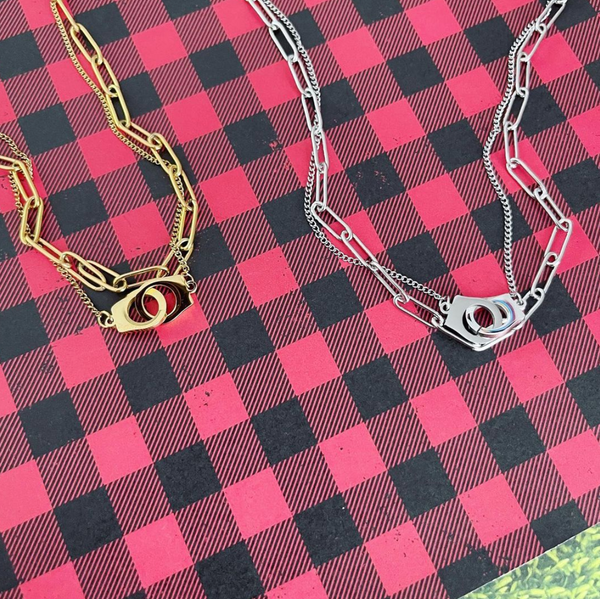 This is an image of our gold and silver layered handcuff necklaces on a red and black plaid background