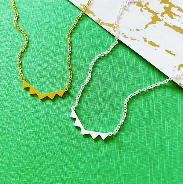 This is an image of our gold and silver minimalist triangle necklace on a green and marble background