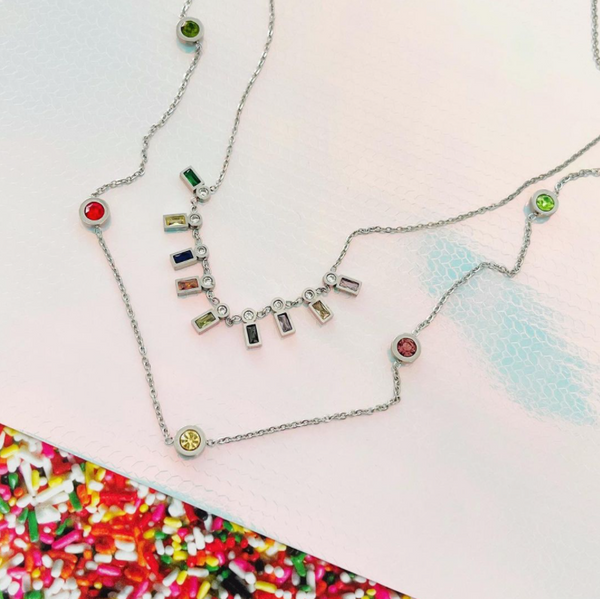 This is an image of our hanging jewel tone necklace with our long layering jewel tone necklace a shimmer background