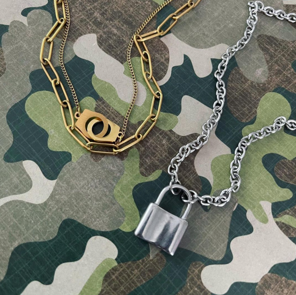 This is an image of our gold layered handcuff necklace with our silver bold lock necklace on a camo background