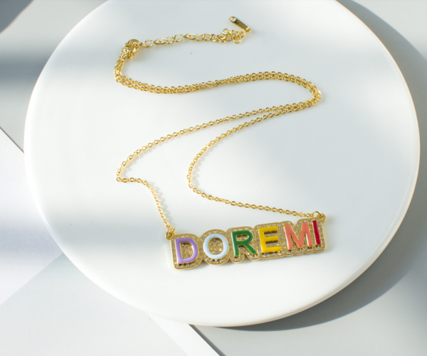 This is an image of our gold rainbow iced nameplate necklace on a white backgrounnd