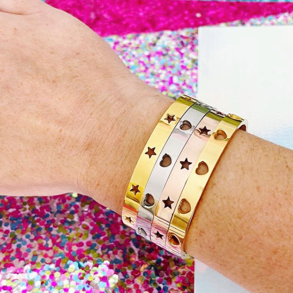 This is an image of our star struck and heart punched bangles worn in an arm party on a glitter background