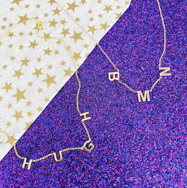 This is an image of our hanging name necklaces on a purple glitter background that read Hugh and BMN