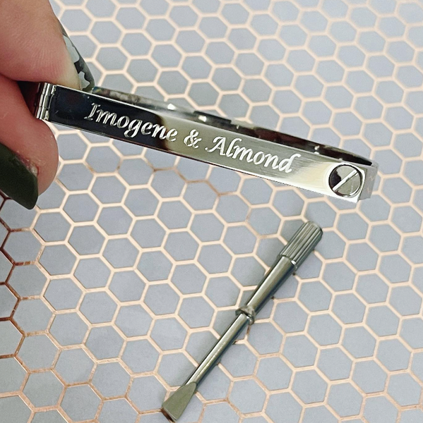 This is an image of our silver personalized screw bangle bracelet that says Imogene & Almond with a screw driver on a honeycomb background