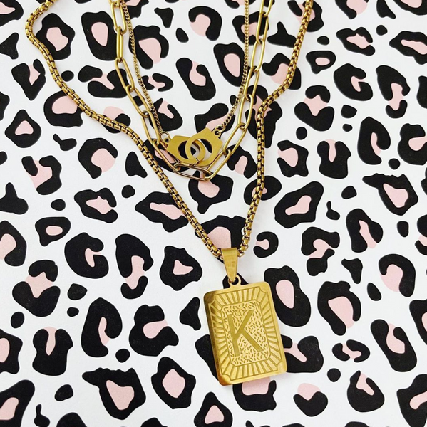 Gold layered handcuff necklace with a rectangle madallion necklace on a pink and black leopard background